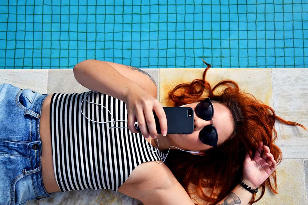 woman laying down next to swimming pool using her mobile phone to share content with friends